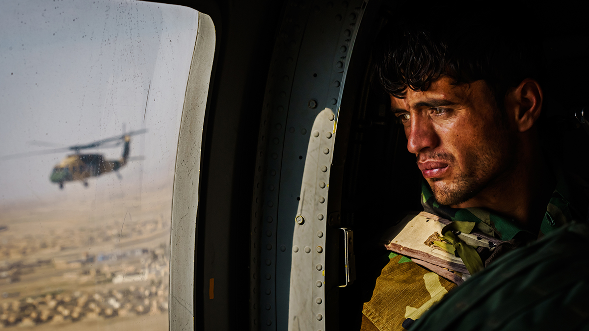 This 2021 photo by photojournalist Marcus Yam was part of Yam’s Pulitzer Prize-winning coverage of the U.S. withdrawal from Afghanistan. It shows a soldier surveying the terrain out of the window of a UH-60 Black Hawk during a resupply flight toward an outpost in the Shah Wali Kot district north of Kandahar, Afghanistan, on May 6. Since the U.S. withdrawal, the Taliban have overpowered government troops, further denying Afghan security forces the use of roads. All logistical support to thousands of outposts and checkpoints — including re-supplies of ammunition and food, medical evacuations, or personnel rotation — must be done by air. Yam is the symposium’s keynote speaker. | Photo: Marcus Yam