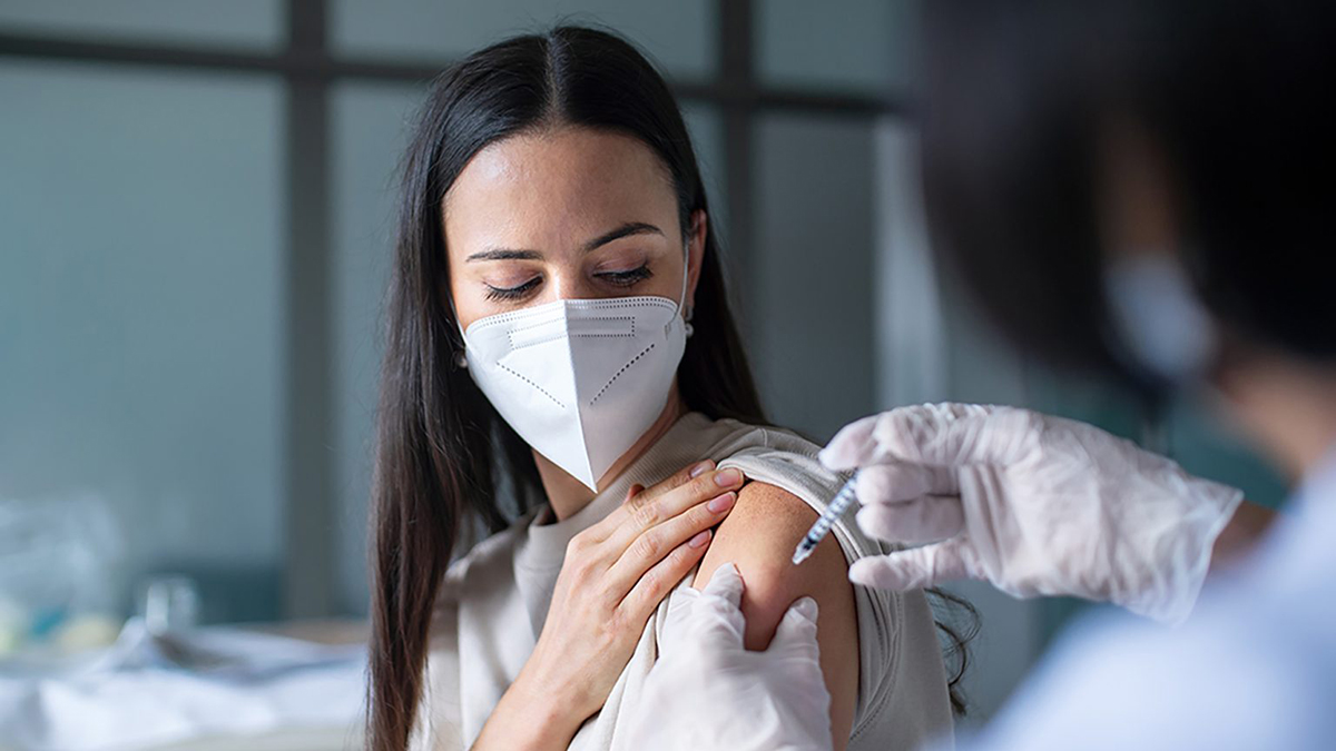 Woman wearing a medical mask receives an injection in her arm
