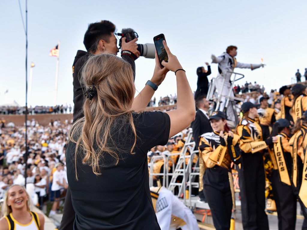 Taylor Holmes, foreground, records smartphone video of Marching Mizzou during a timeout at the Mizzou vs. Buffalo football game Sept. 7, 2024, in Memorial Stadium. To her left is Chris Wang, M2 media coordinator.