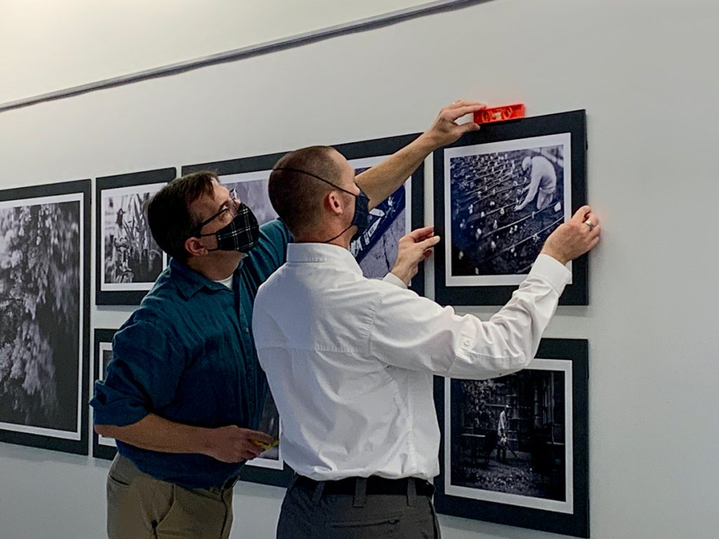 Lynden Steele, left, director of photojournalism at Reynolds Journalism Institute, and doctoral student Cory MacNeil install MacNeil's groundskeepers photo series Oct. 19, 2021, in the RJI lobby. As reported in the Columbia Missourian, MacNeil spent weeks shadowing the groundskeepers who care for the Mizzou Botanic Garden, which is the entire Mizzou campus. Photo: Nate Brown