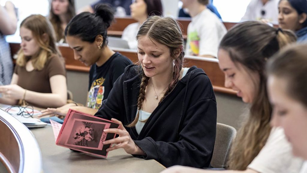 Nichole Fuchs, center, assembles a small handmade art book called a zine, which includes photographs and research that tell a story about the 1960s.