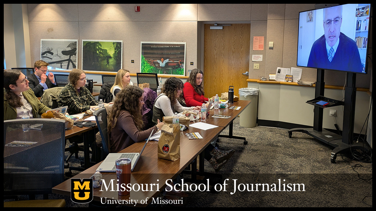 Alex MacGillis appears on a TV screen in front of a class of students