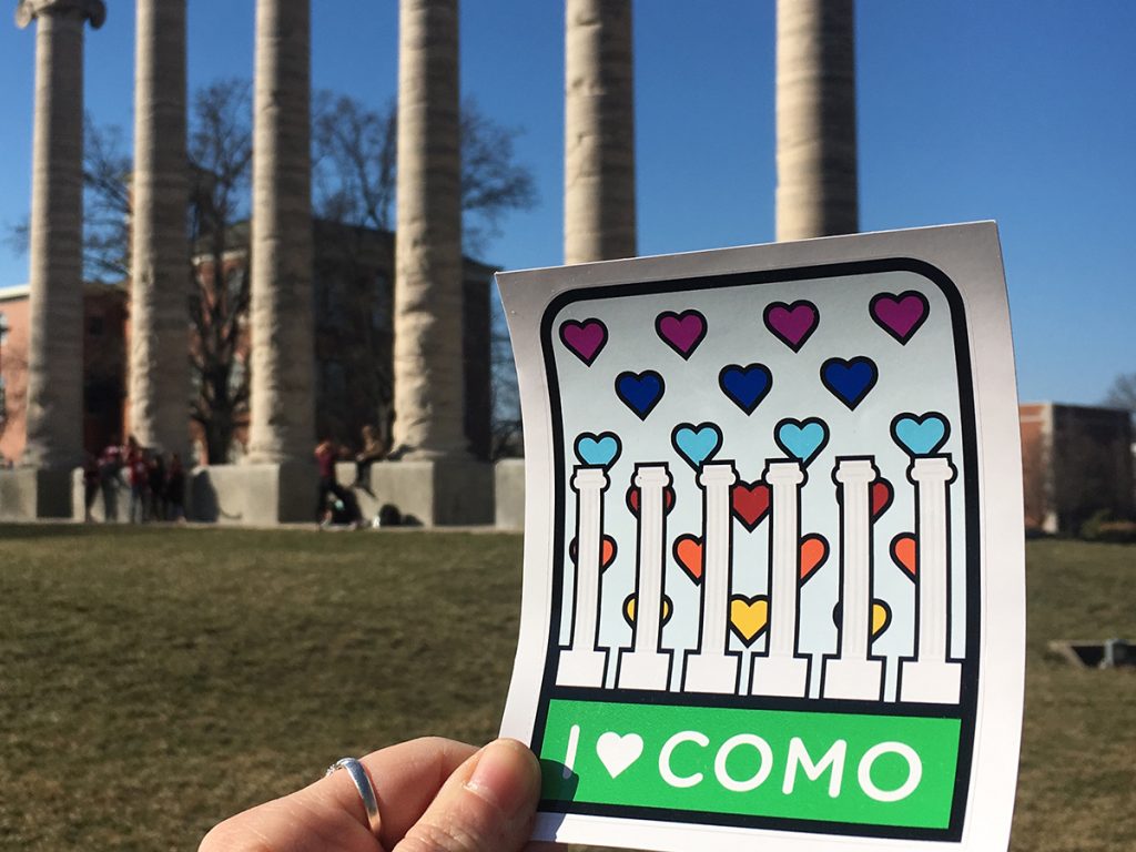 Holding up an I heart COMO sticker in front of the Columns