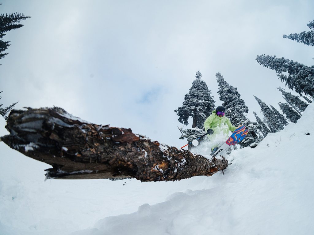Erin Spong skiing over a log on a snow-covered mountain