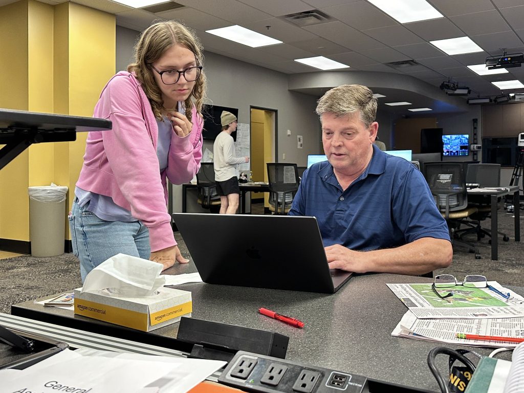 Associate Professor Gordon Dickson, right, the Columbia Missourian local government editor, reviews an election story with junior Sydney Rohrberg in the Missouri News Network newsroom.